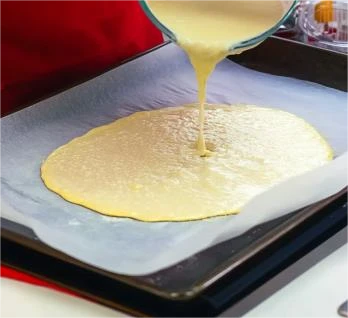 Pouring Cottage Cheese Flatbread Batter Pouring blended cottage cheese flatbread batter onto a parchment-lined tray